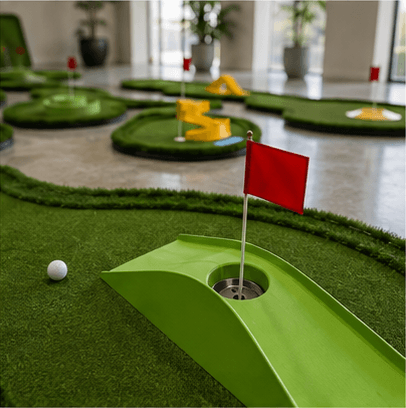 Indoor mini golf hole with red flag and golf ball on green turf