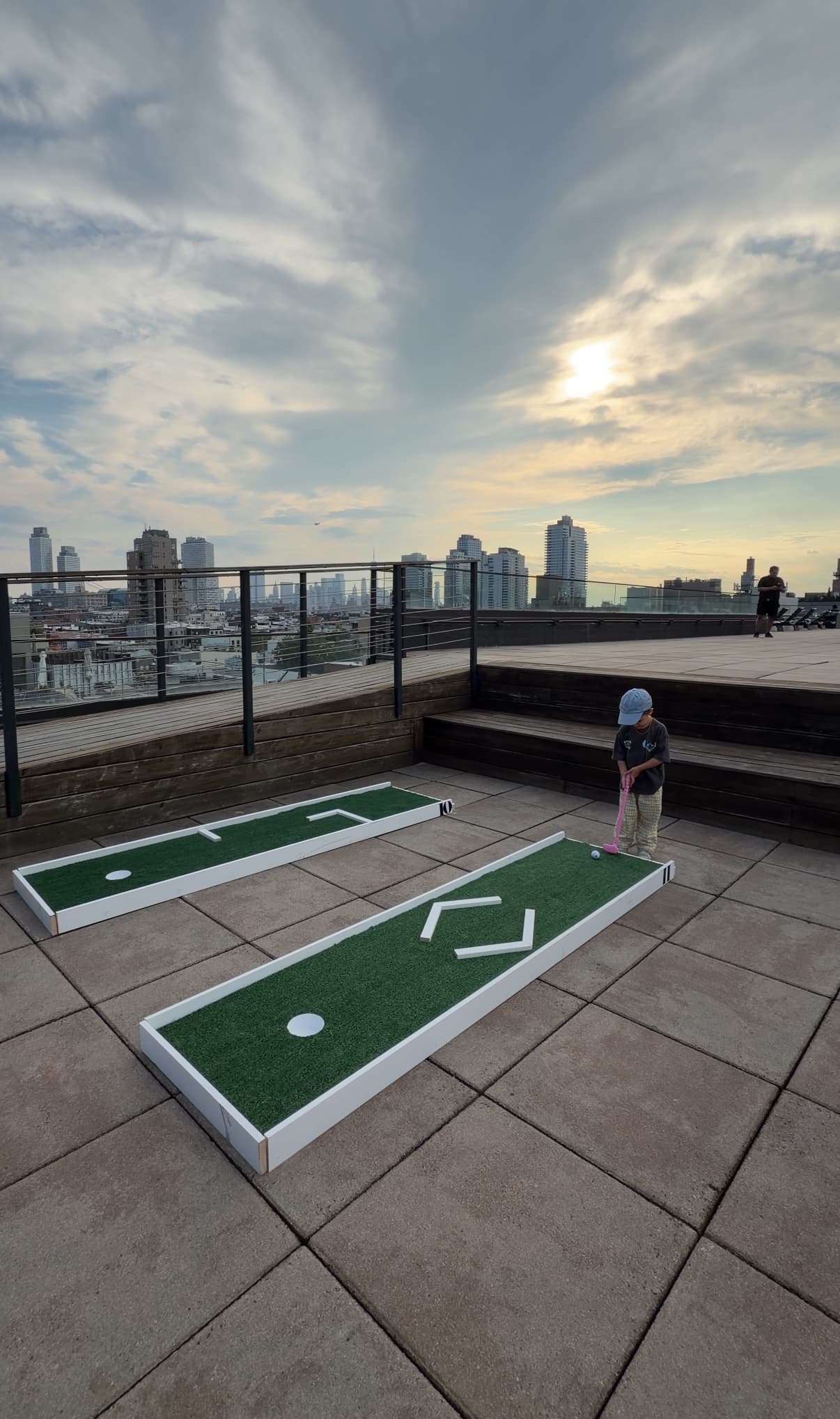Child playing mini golf on a rooftop terrace with city skyline